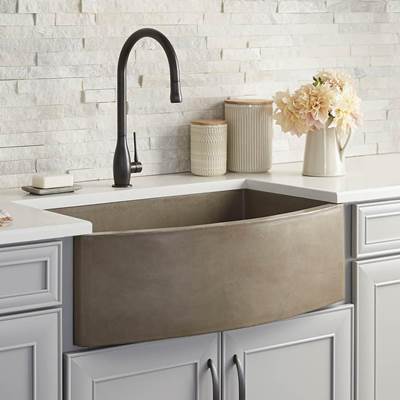 Earth-toned farmhouse sink with curved front, black faucet, and white subway tile backsplash in kitchen setting.
