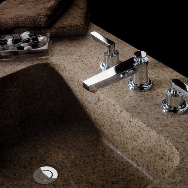 Polished chrome lavatory faucet with spout and dual handles mounted on speckled stone countertop with integrated sink.