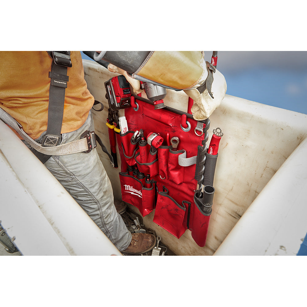 Red canvas tool apron with multiple pockets and metal rings worn by worker on utility pole.