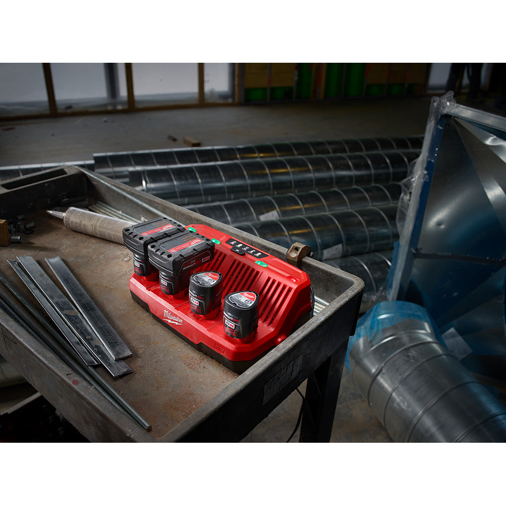 Red Milwaukee M12 four-bay sequential charger with two batteries installed, positioned on a work table.
