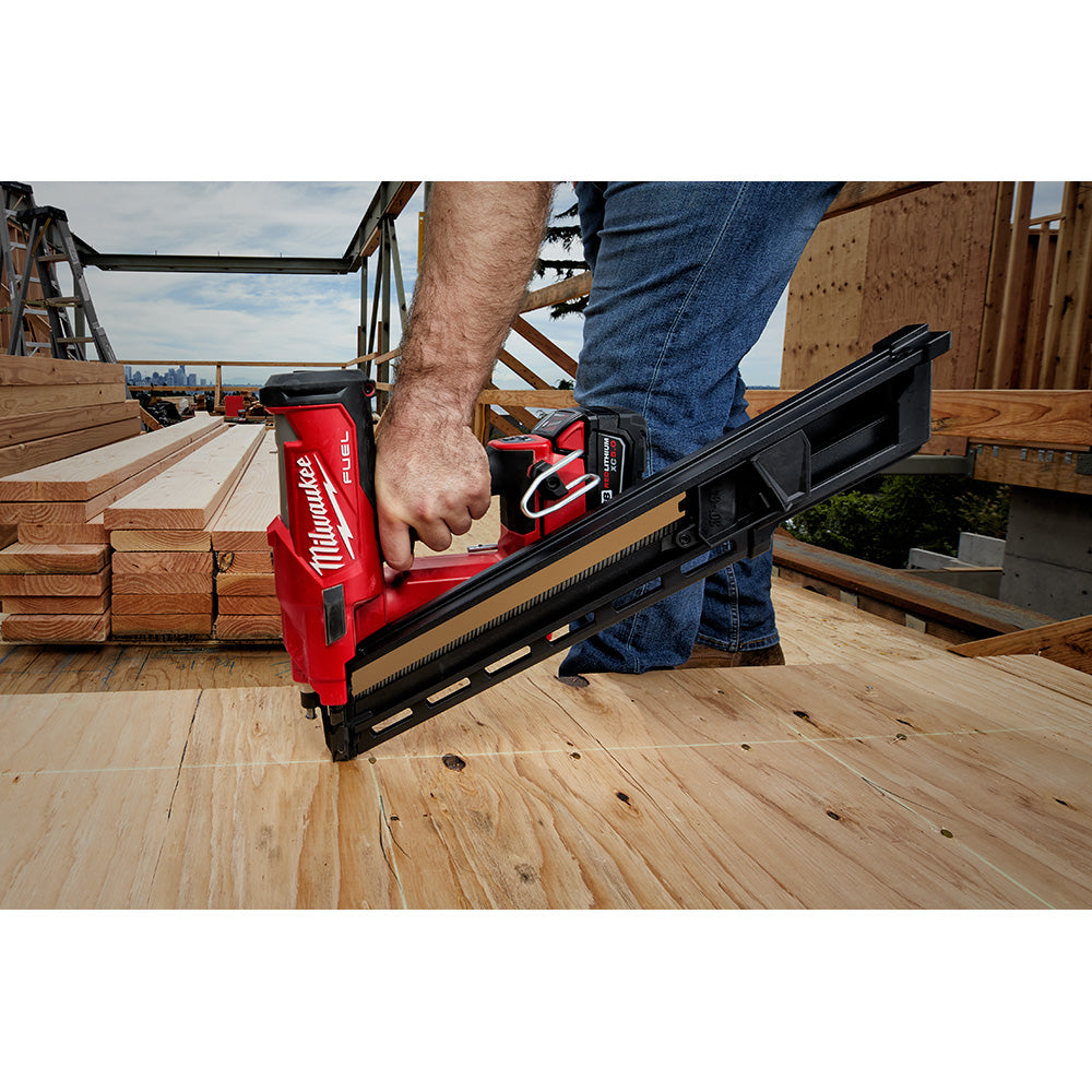Red and black Milwaukee M18 FUEL framing nailer with extended magazine being held on wooden decking at a construction site.