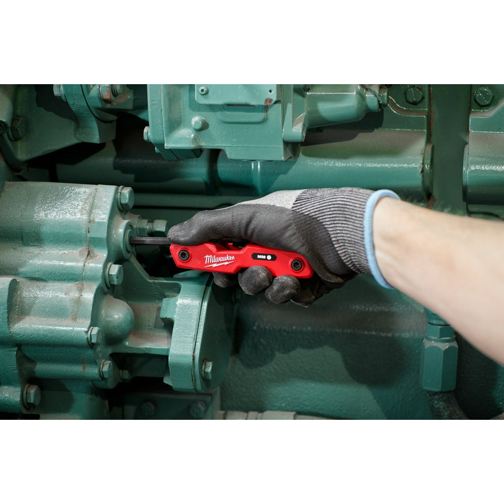 Red folding hex key set with eight metric keys held in hand over machinery.