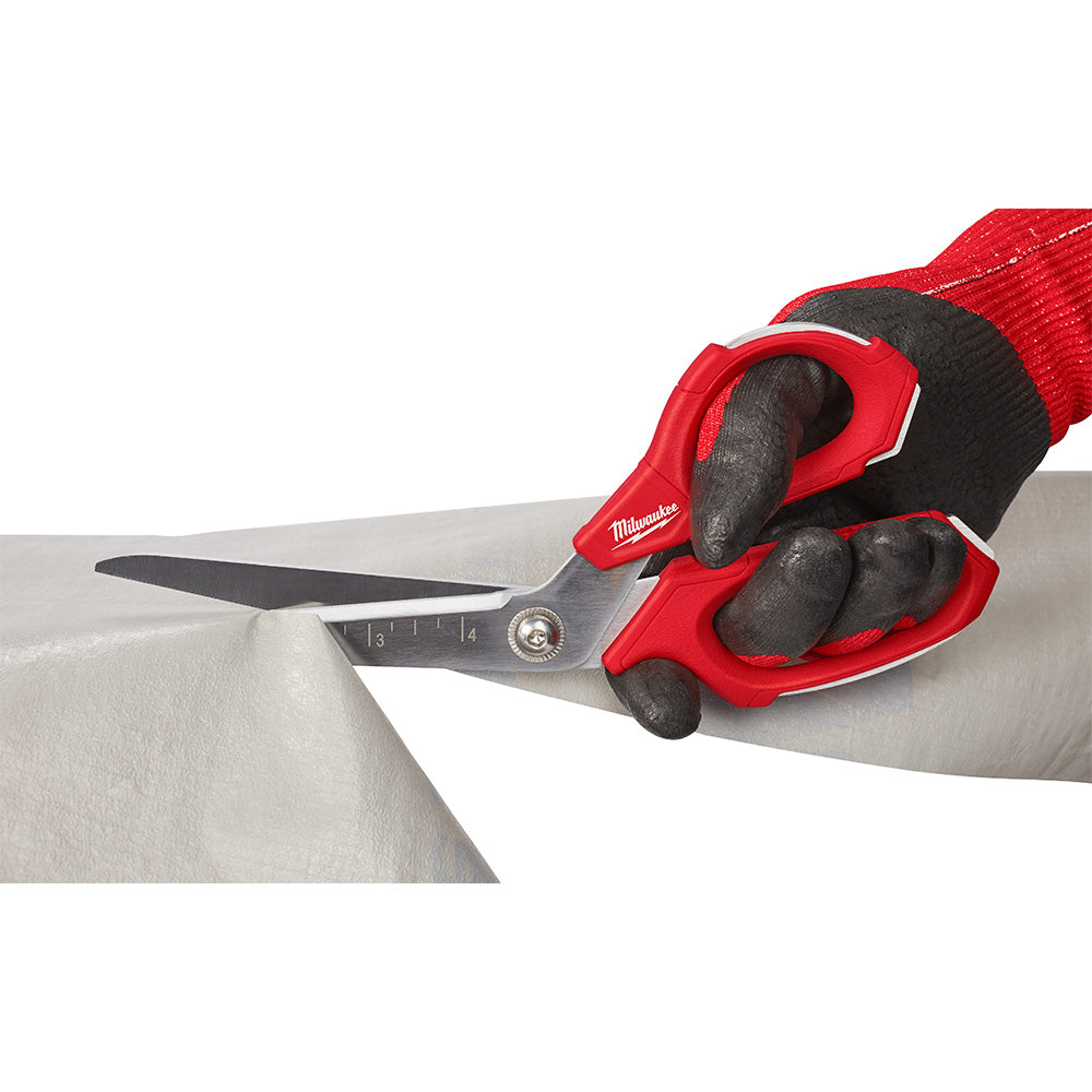 Red and black offset scissors with measurement markings cutting through sheet metal.