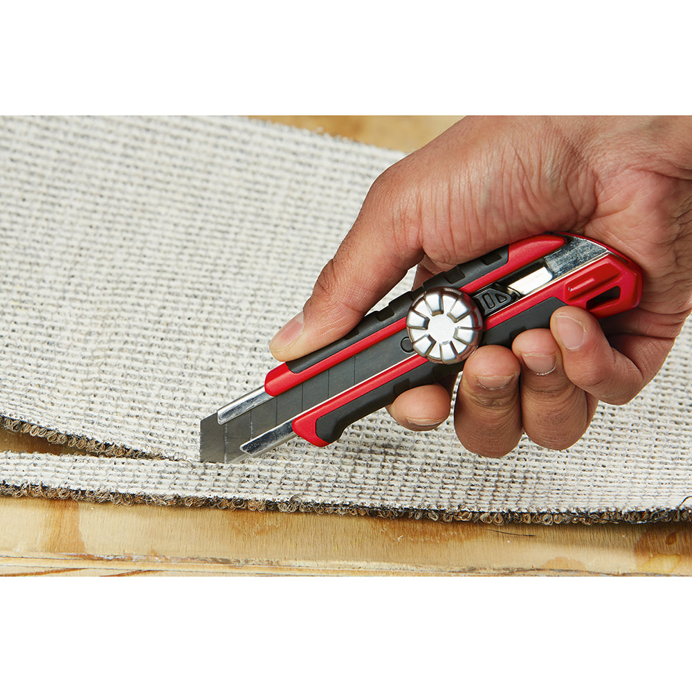 Red and black snap-off utility knife with metal lock mechanism held in hand cutting fabric.