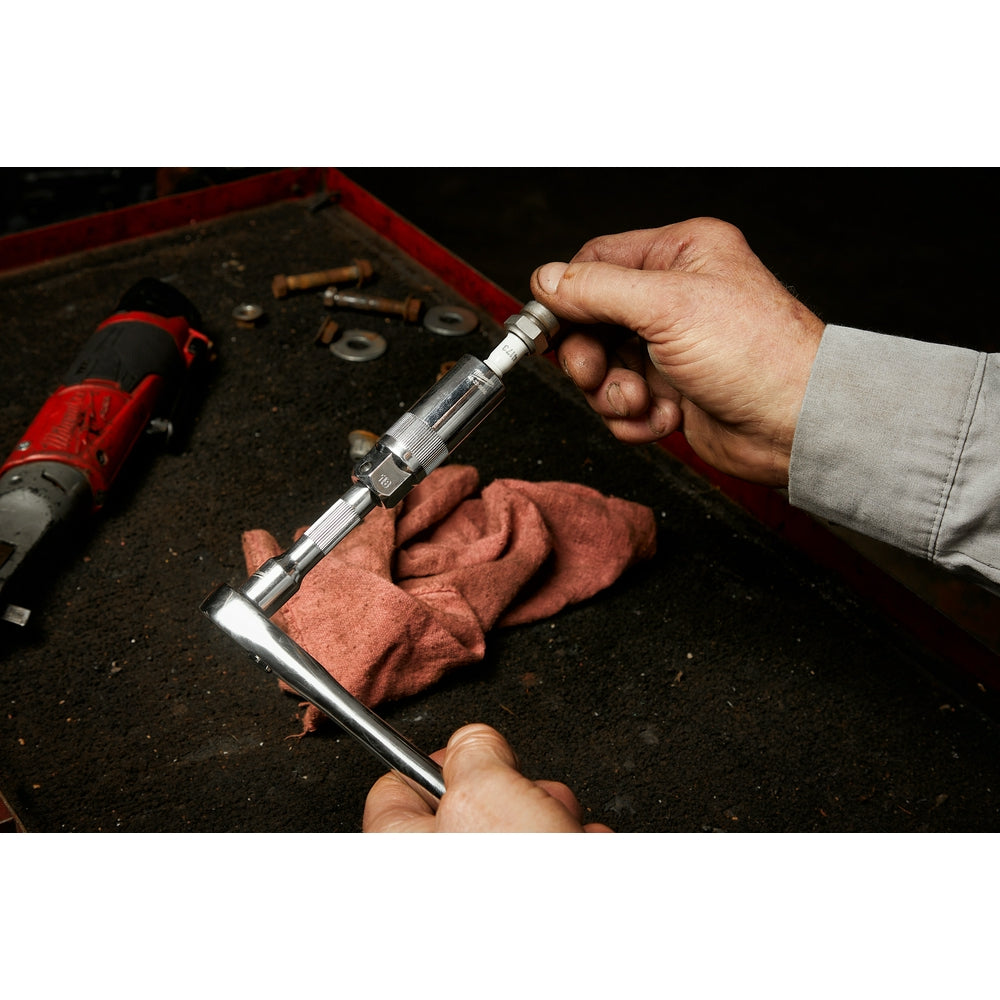 Silver and black spark plug socket with 3/8" drive held in hands over a workbench.