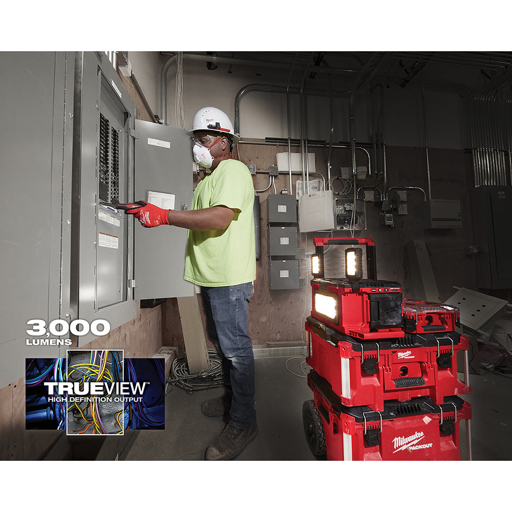 Red Milwaukee M18 PACKOUT work light with illuminated panels stacked on mobile cart in industrial electrical setting.