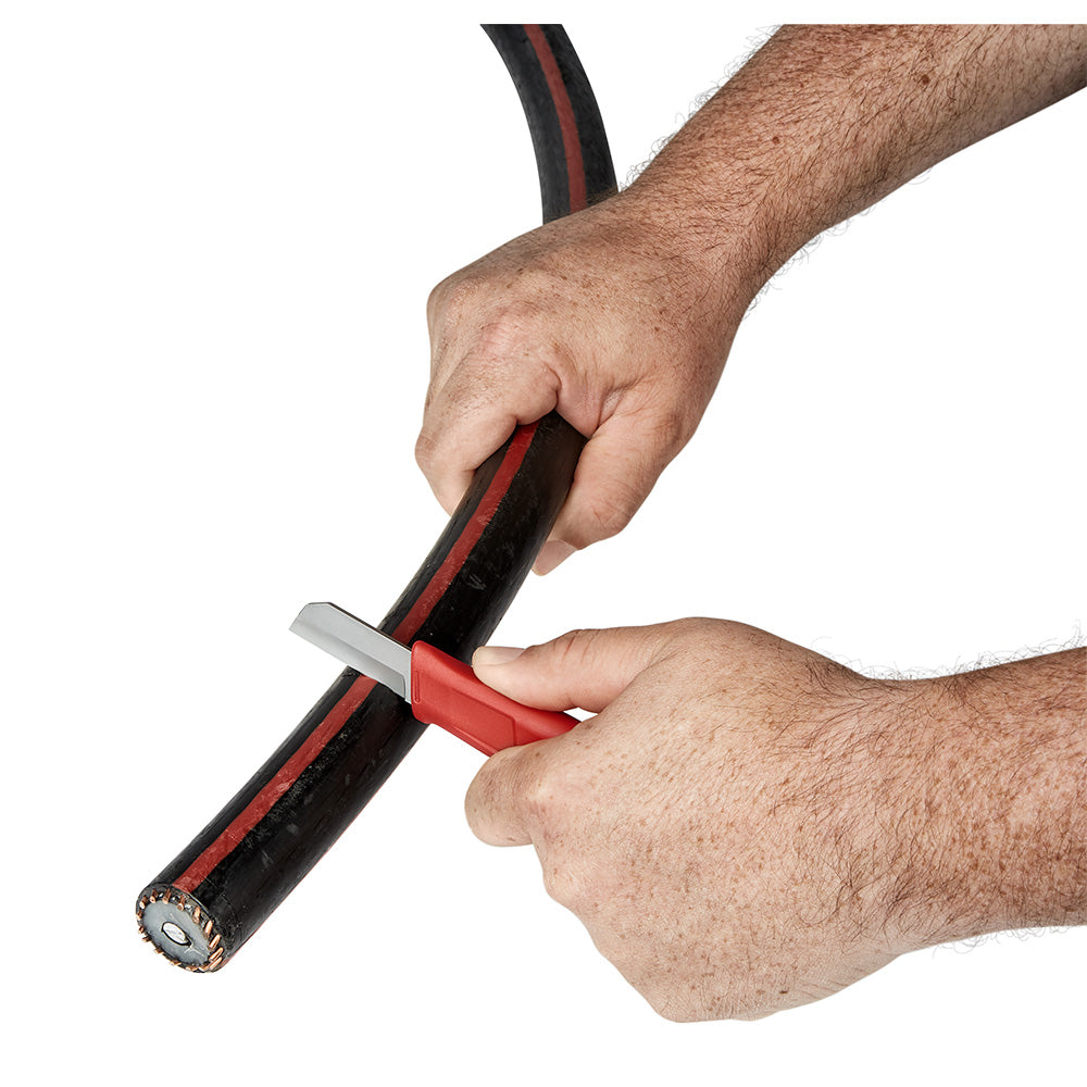 Black and red lineman underground knife with blade cutting through insulated cable, held in both hands.