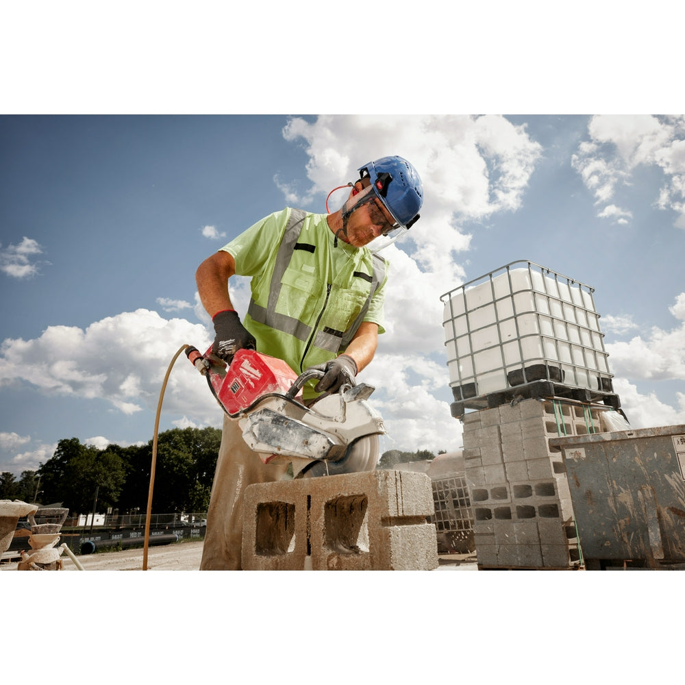 Worker wearing blue helmet with clear face shield attached, cutting concrete block on construction site.