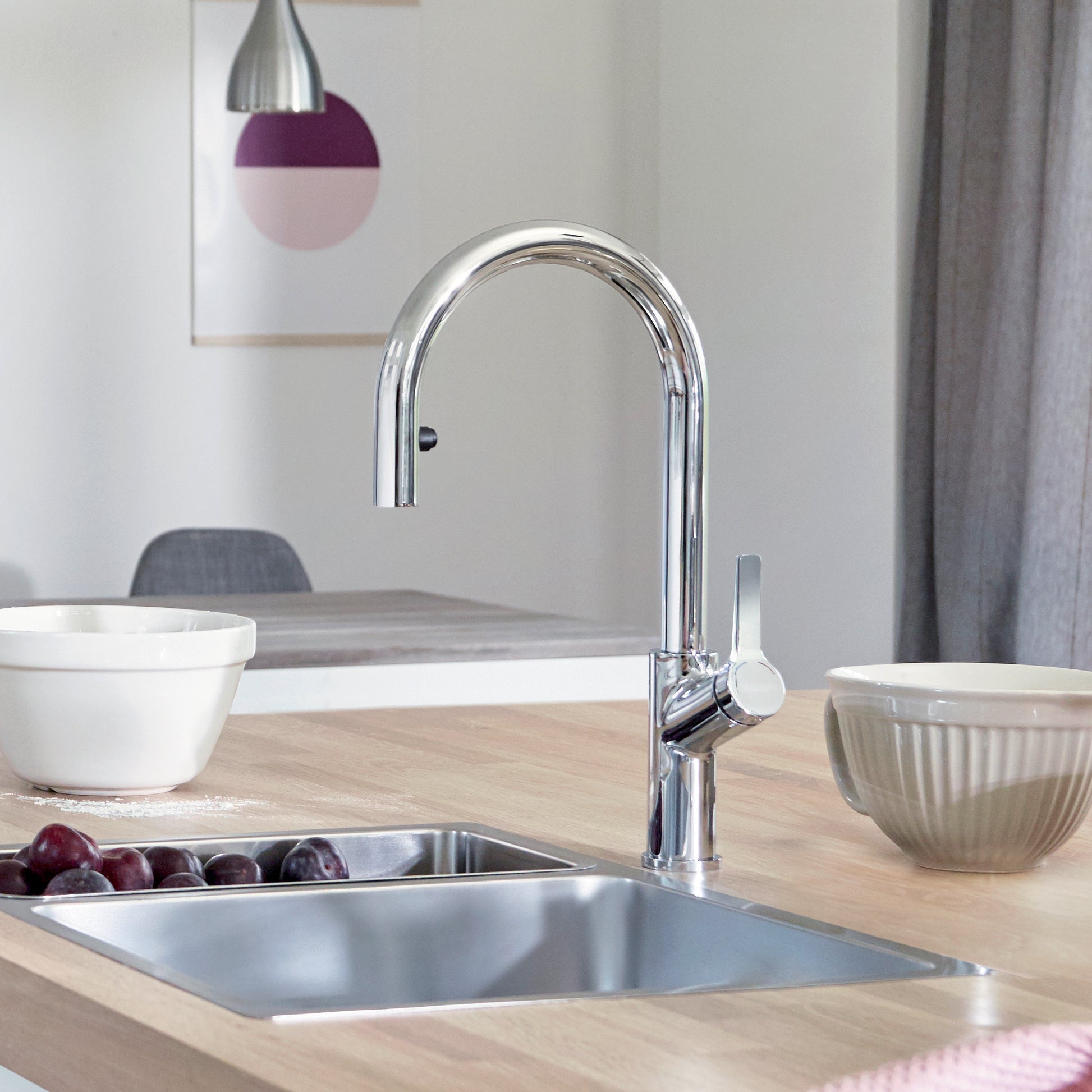 Chrome pull-down kitchen faucet with curved spout and single lever handle mounted above stainless steel sink.