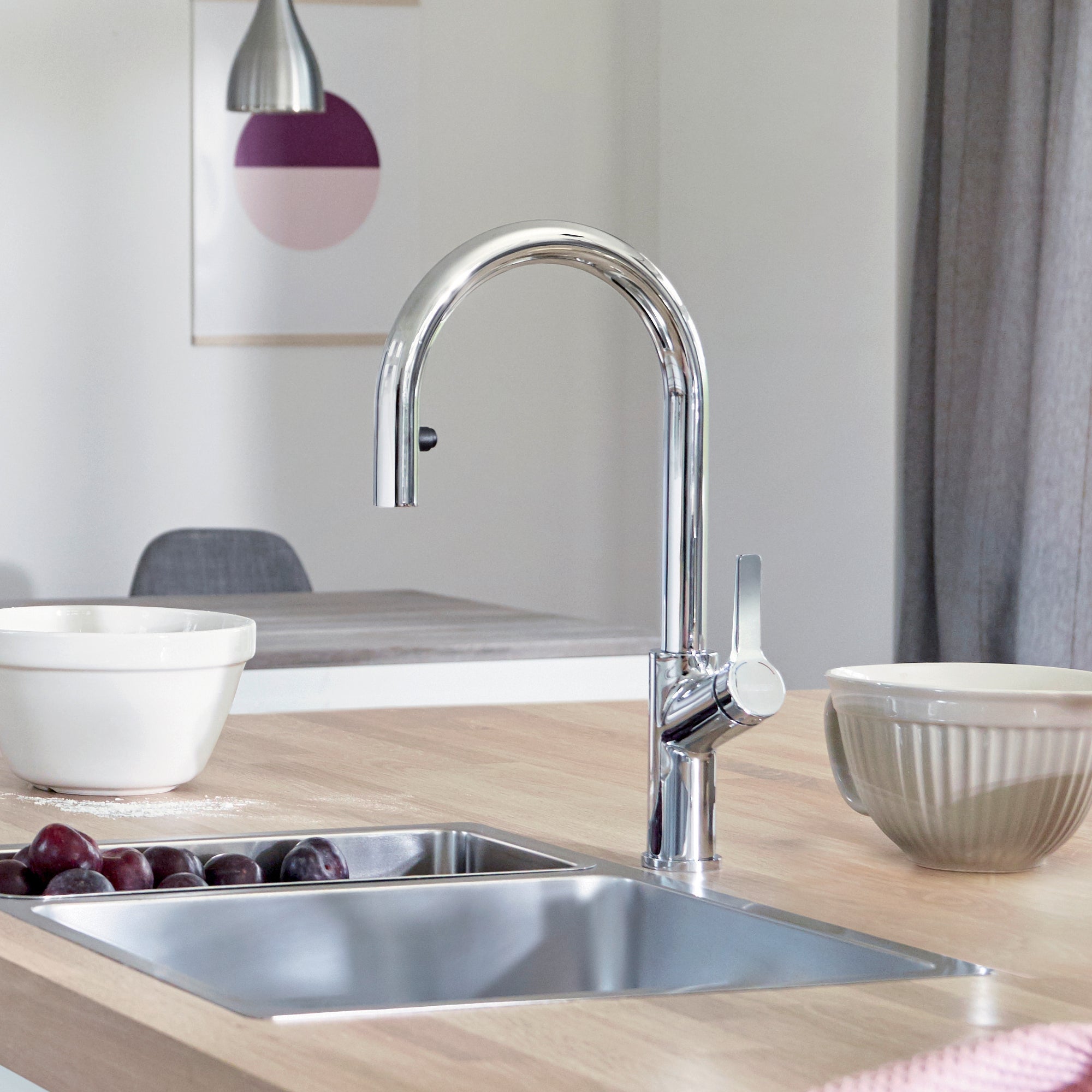 Chrome pull-down kitchen faucet with curved spout and single lever handle mounted above stainless steel sink.
