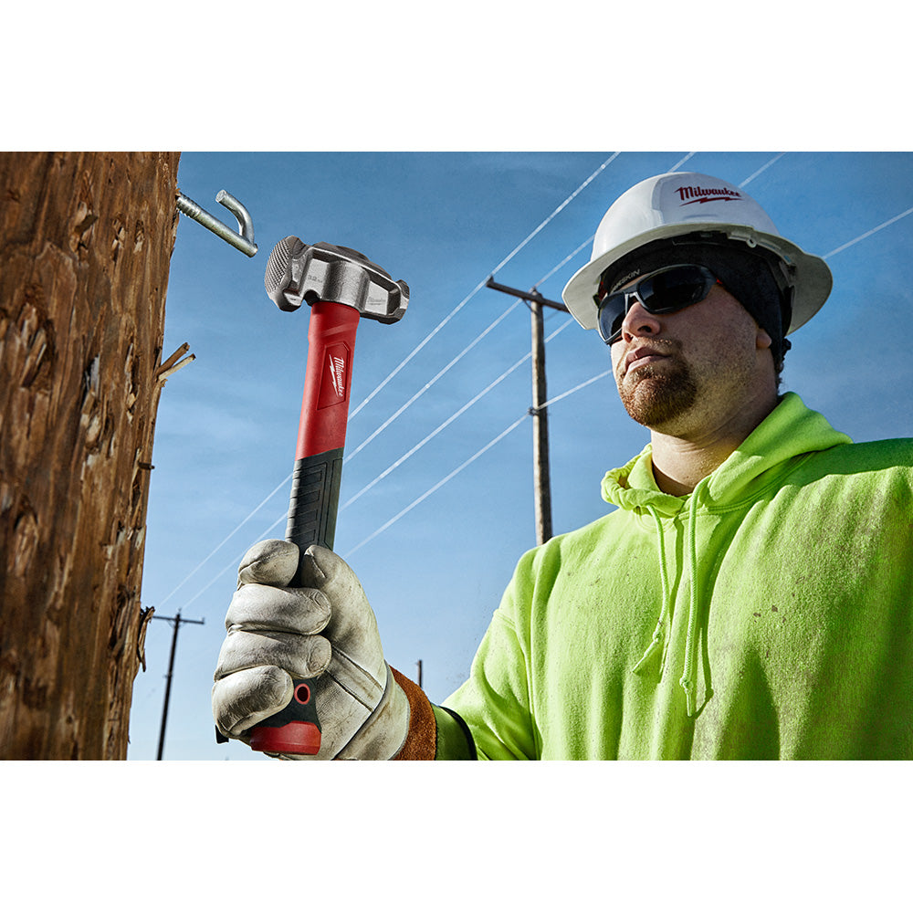 Red and black lineman's hammer with metal head and claw held by worker in safety gear near wooden pole.