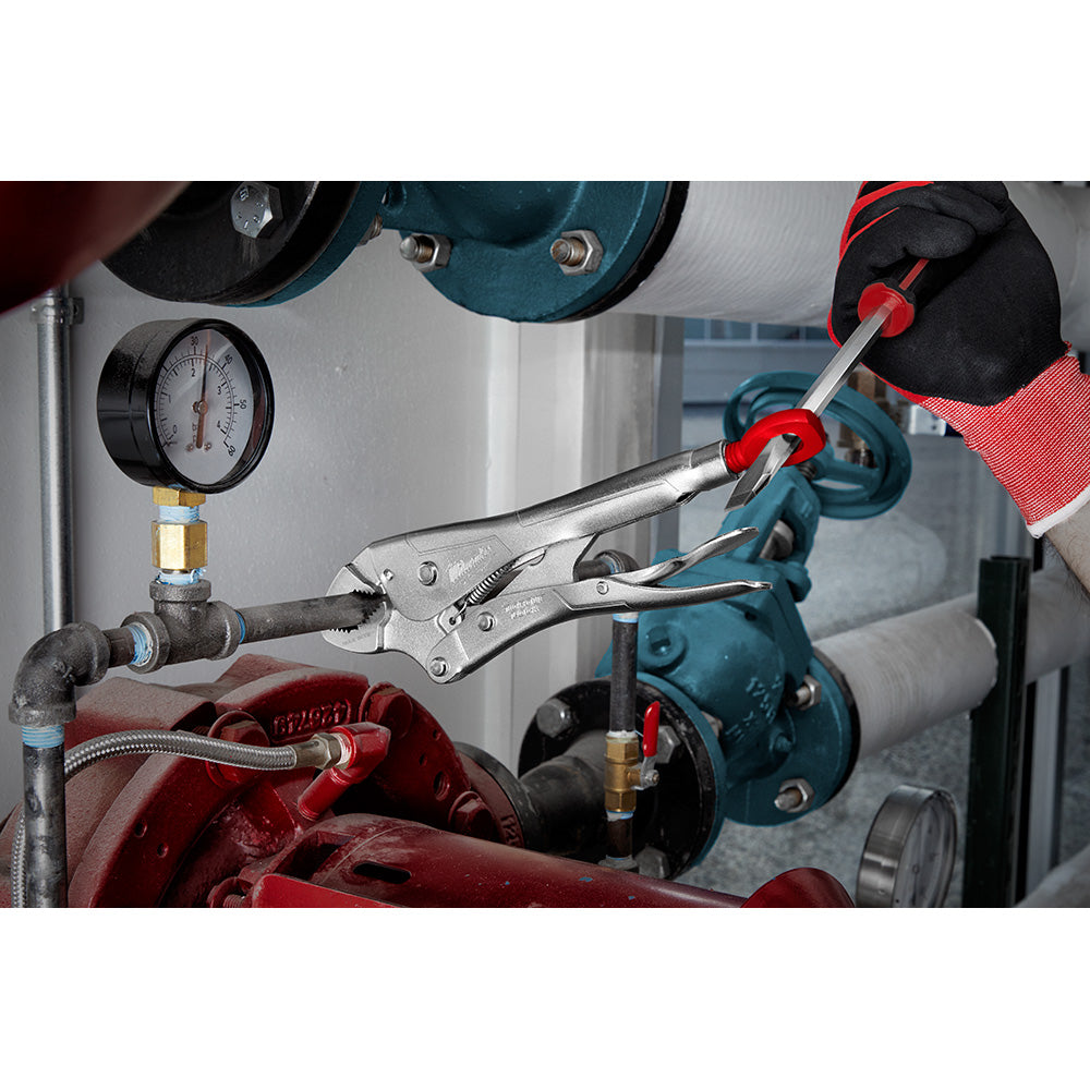 Milwaukee locking pliers with red handles gripping metal pipe in industrial workshop setting.