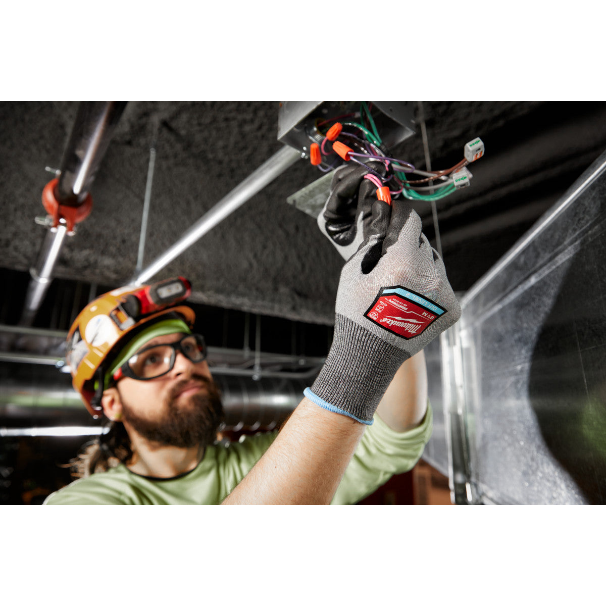 Gray and black polyurethane dipped work gloves with red label worn while handling electrical wiring.