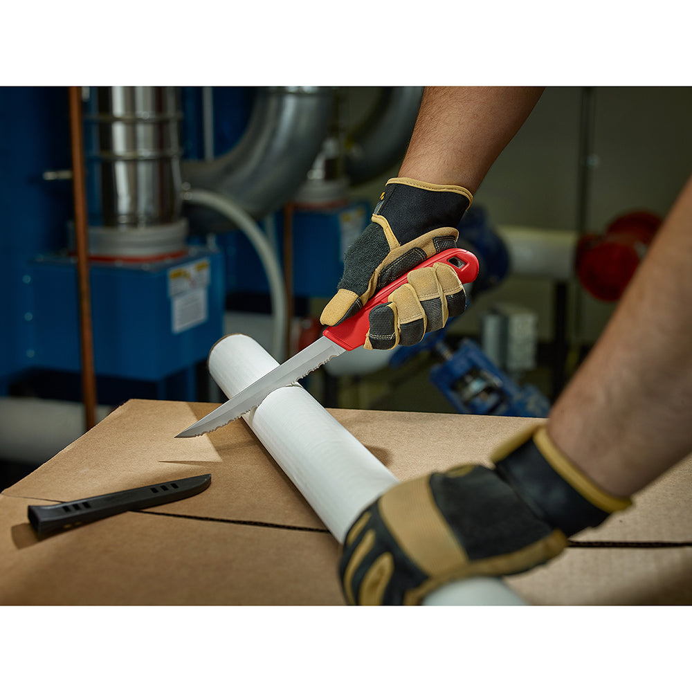 Serrated insulation knife with red handle being used to cut white pipe insulation on cardboard surface.