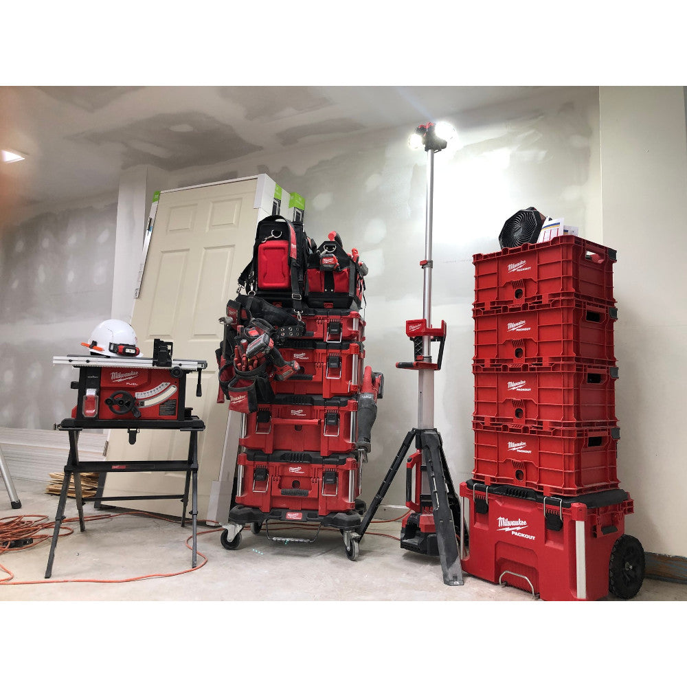 Red Milwaukee PACKOUT crate with grid pattern, handles, and latches stacked with other storage containers in workshop.