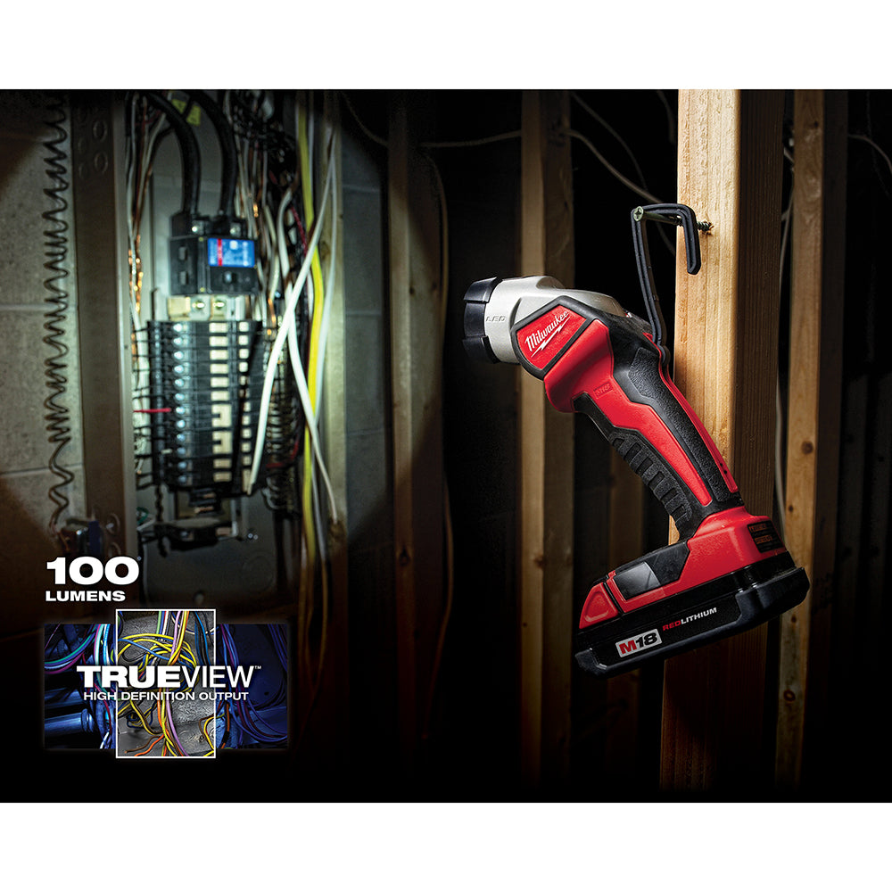Red and black Milwaukee M18 LED work light held at an angle, illuminating an electrical panel in a dark interior space.