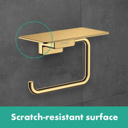 Brushed bronze toilet paper holder with shelf mounted on gray tile wall.