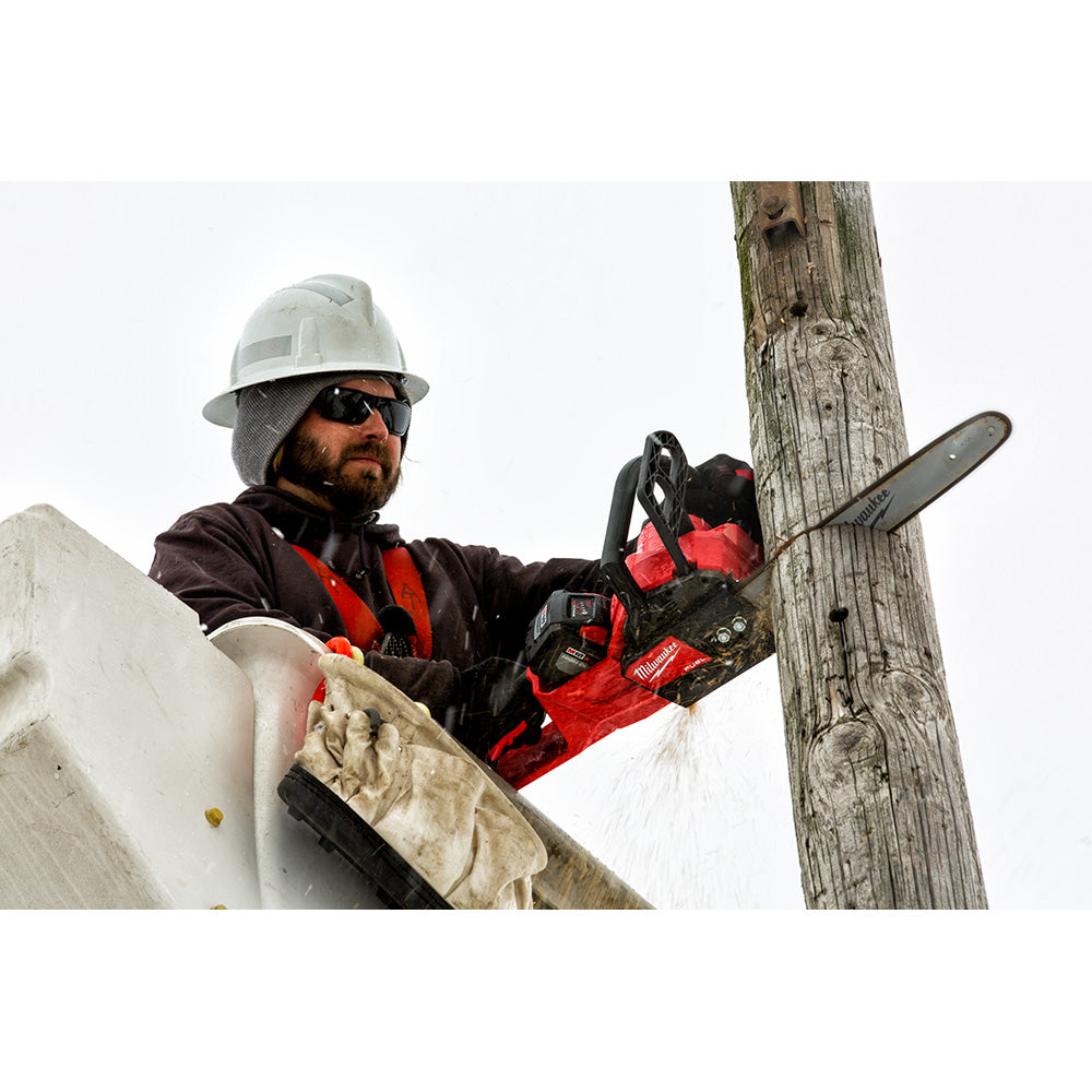 Worker holding red and black chainsaw with 16-inch bar against wooden pole.