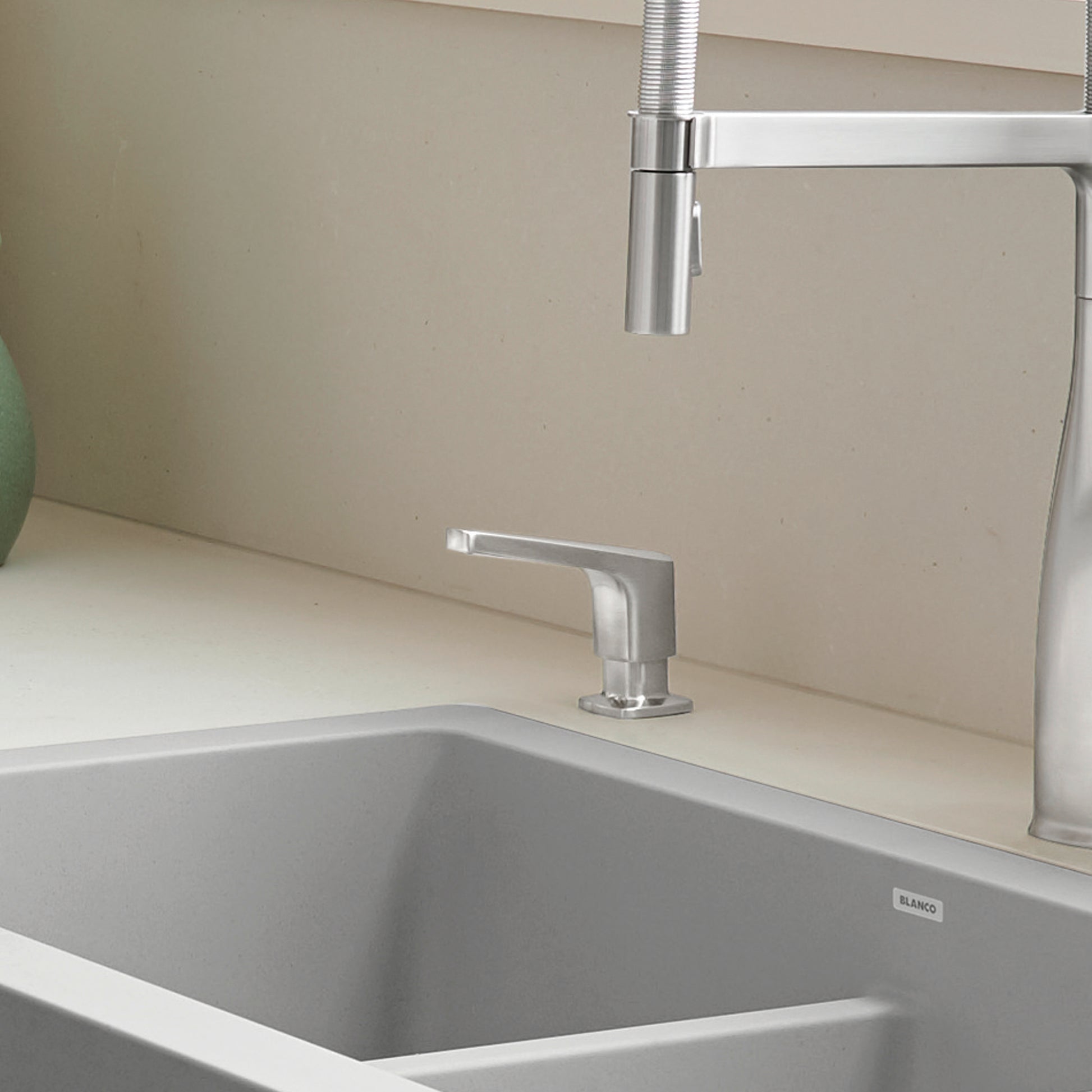 Stainless steel soap dispenser with rectangular pump mounted on kitchen sink countertop next to faucet.