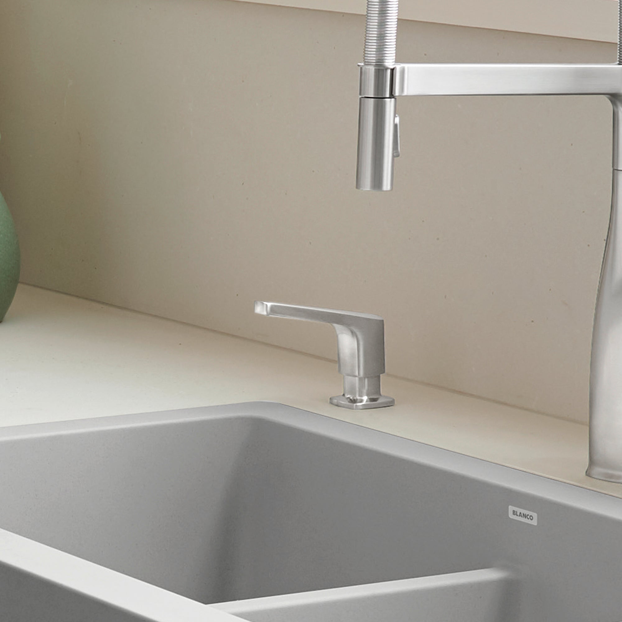 Stainless steel soap dispenser with rectangular pump mounted on kitchen sink countertop next to faucet.