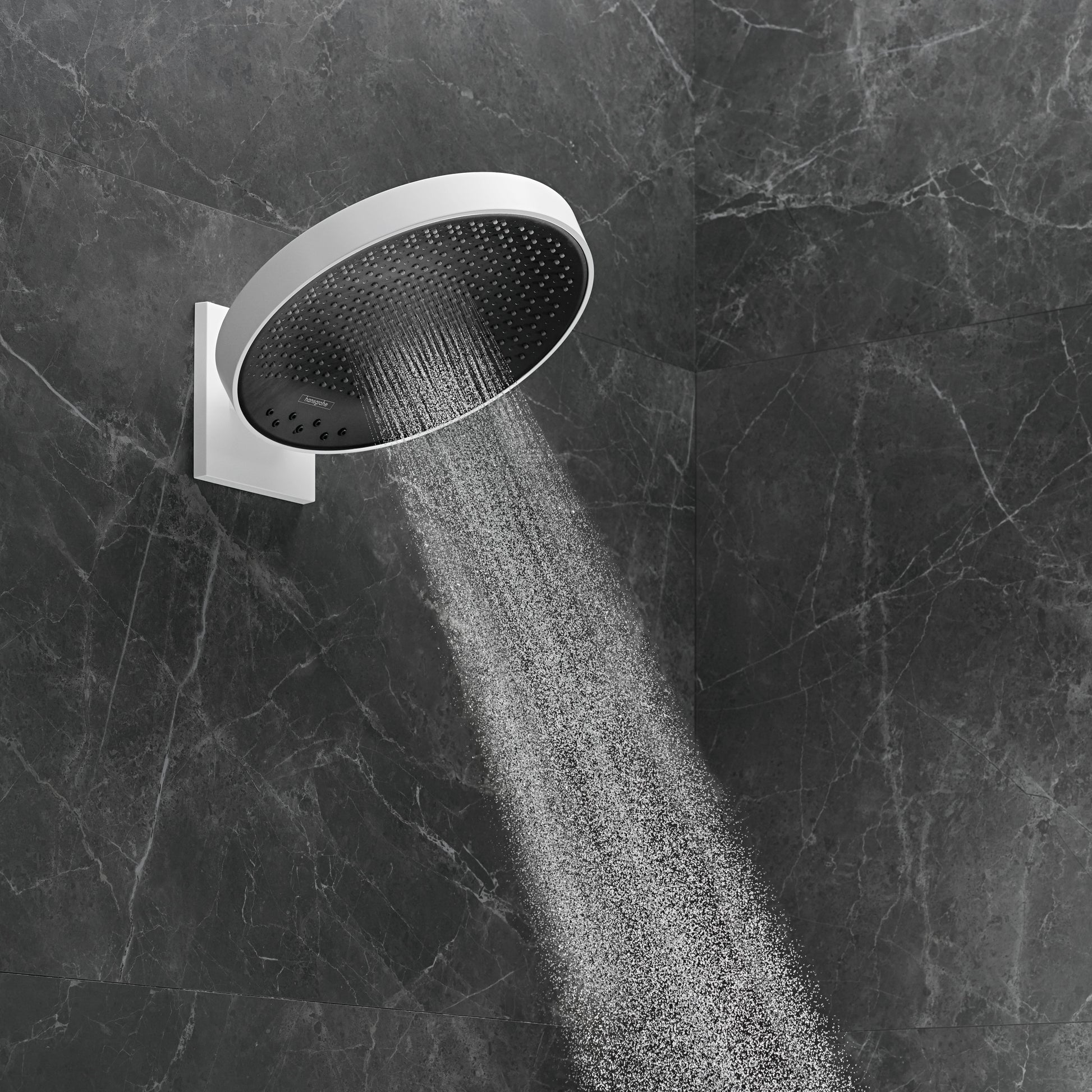 Matte white circular shower head with black perforated faceplate mounted on wall bracket, dispensing water stream against dar