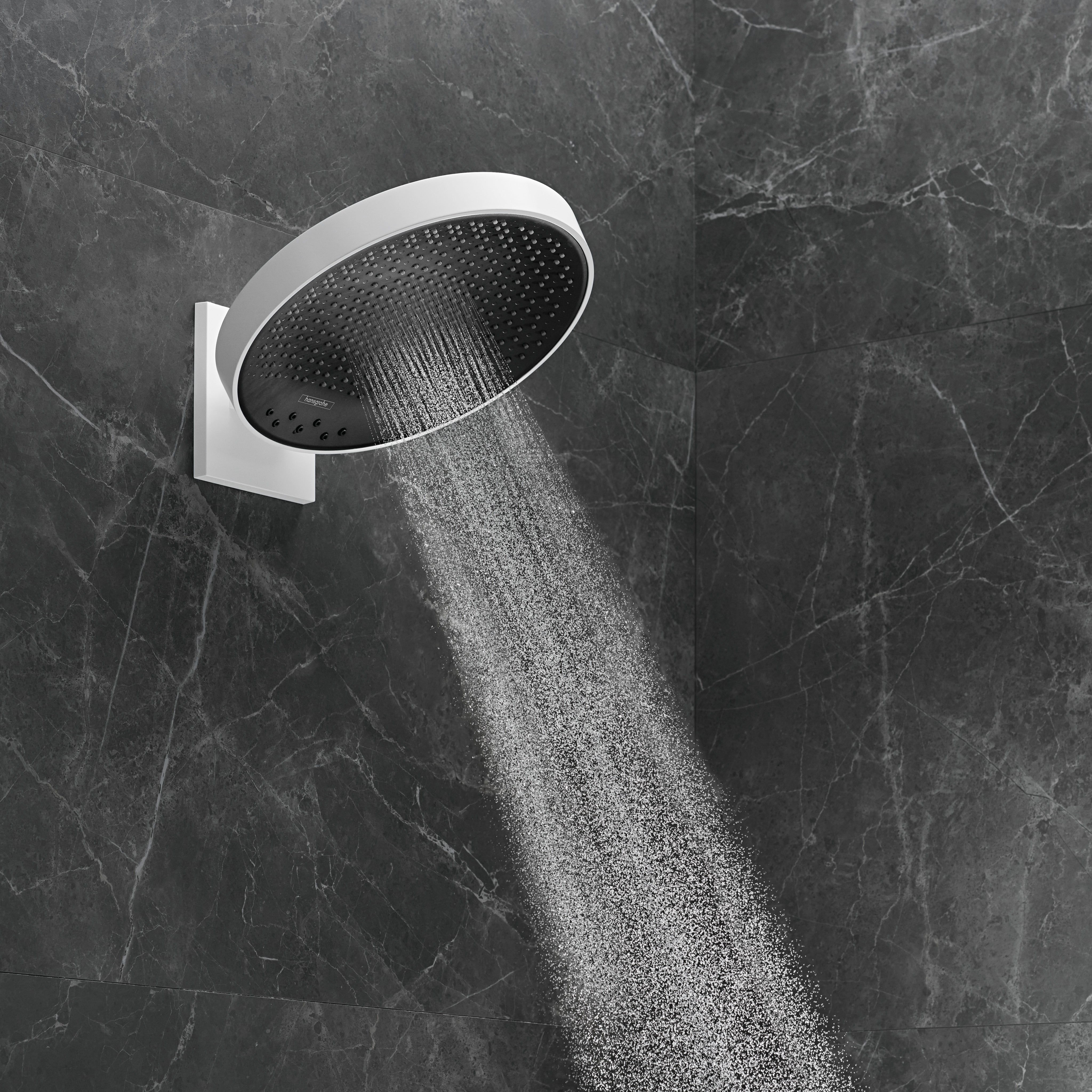Matte white circular shower head with black perforated faceplate mounted on wall bracket, dispensing water stream against dar