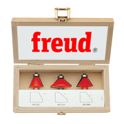 Three red chamfer router bits with metal shanks in a wooden Freud storage box.
