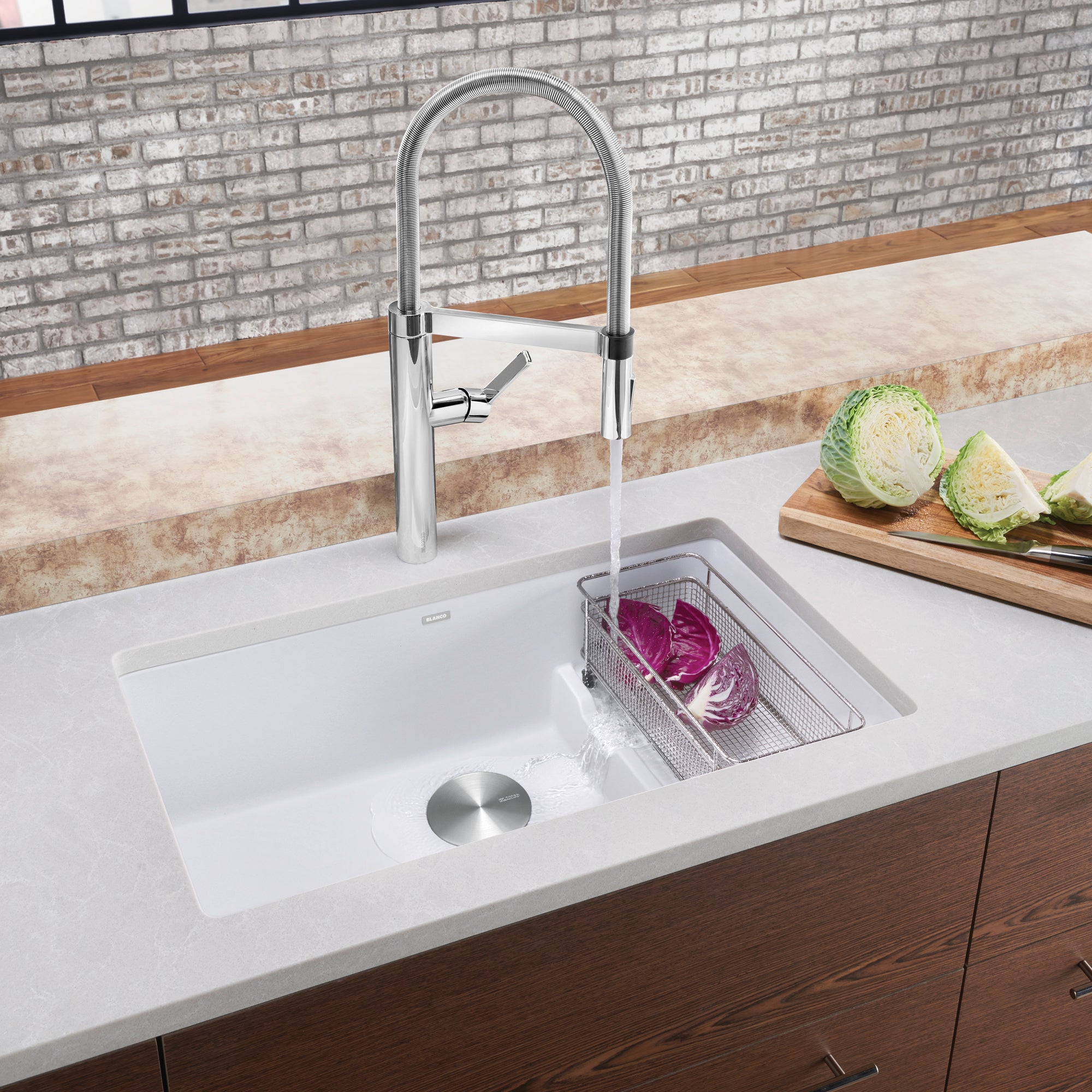 White undermount kitchen sink with arched chrome faucet and strainer basket installed in countertop.