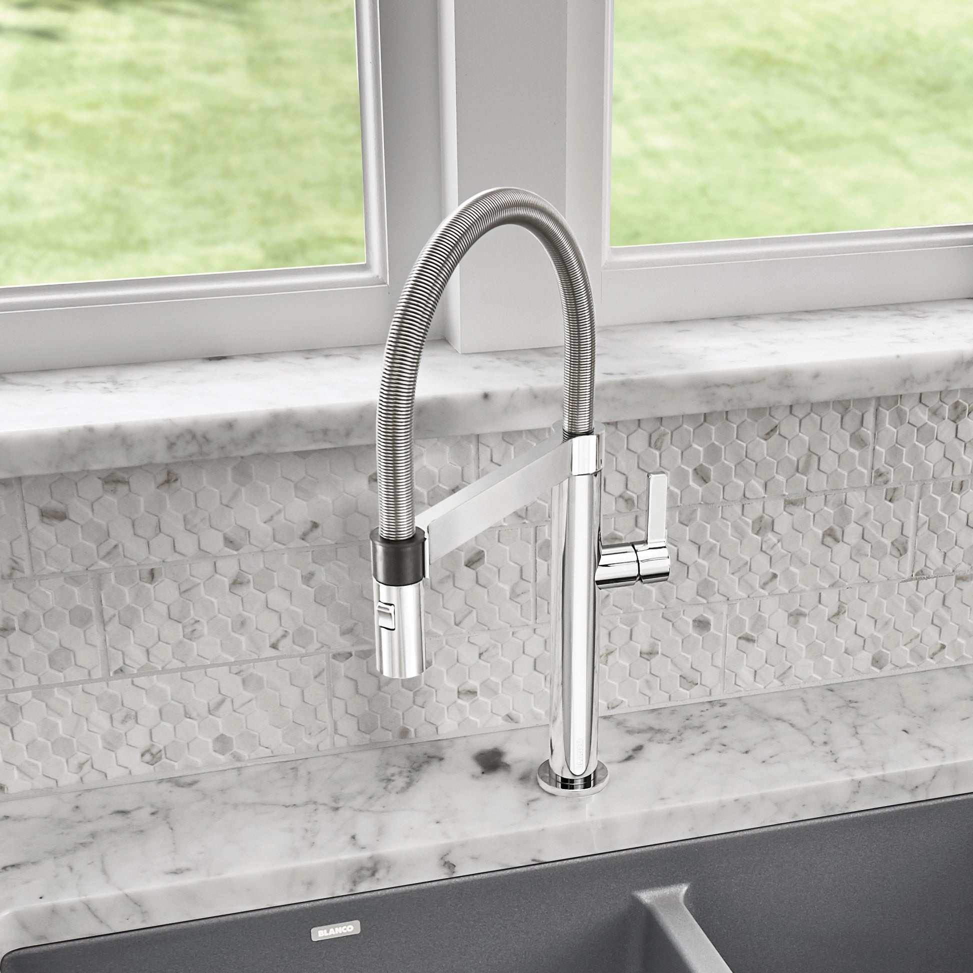 Chrome pull-down kitchen faucet with flexible hose and black grip accent installed above sink.