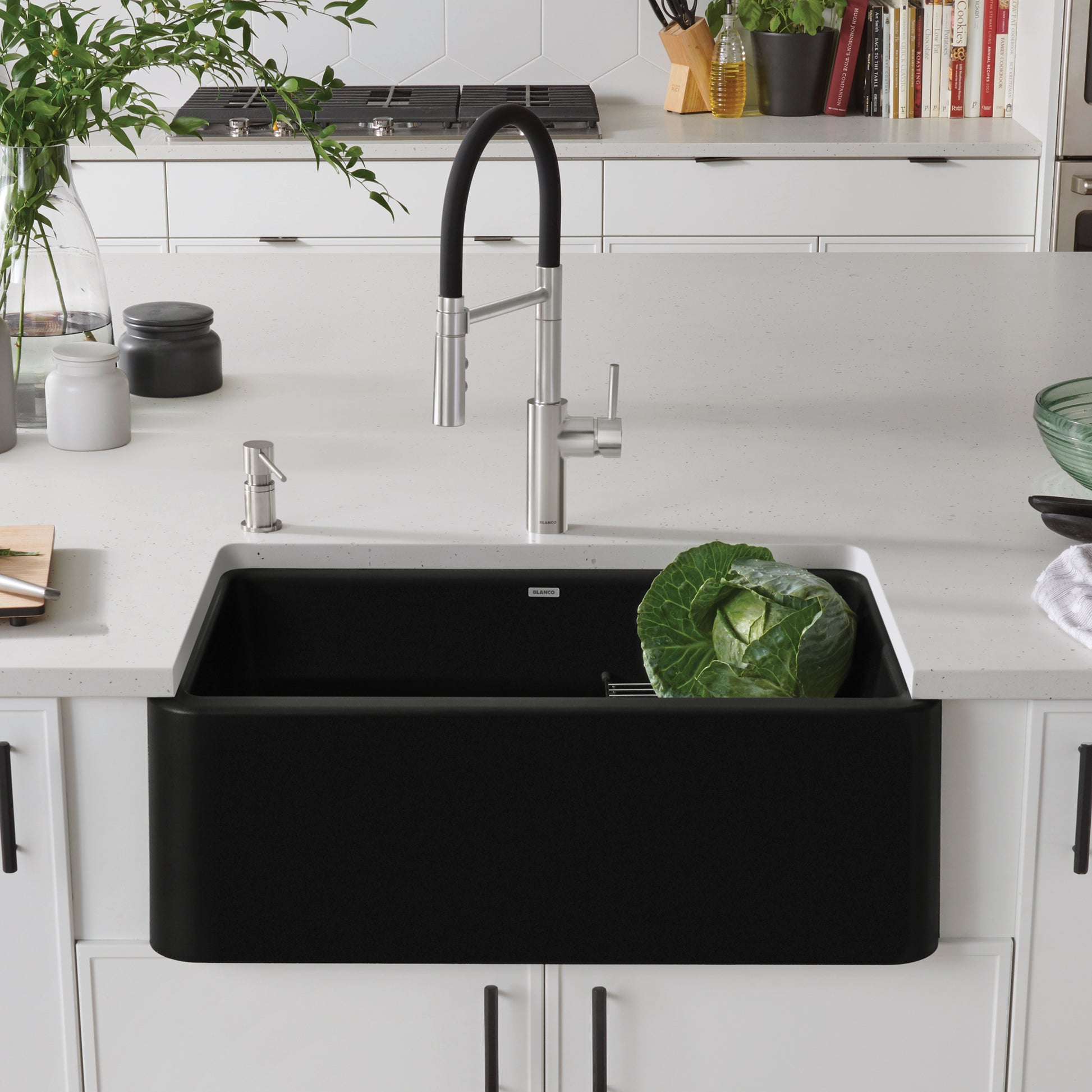 Coal black single bowl farmhouse sink with curved apron front installed in white kitchen cabinetry with stainless steel fauce