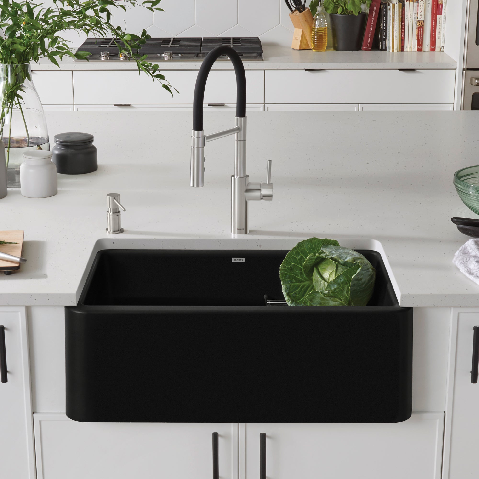 Coal black single bowl farmhouse sink with curved apron front installed in white kitchen cabinetry with stainless steel fauce