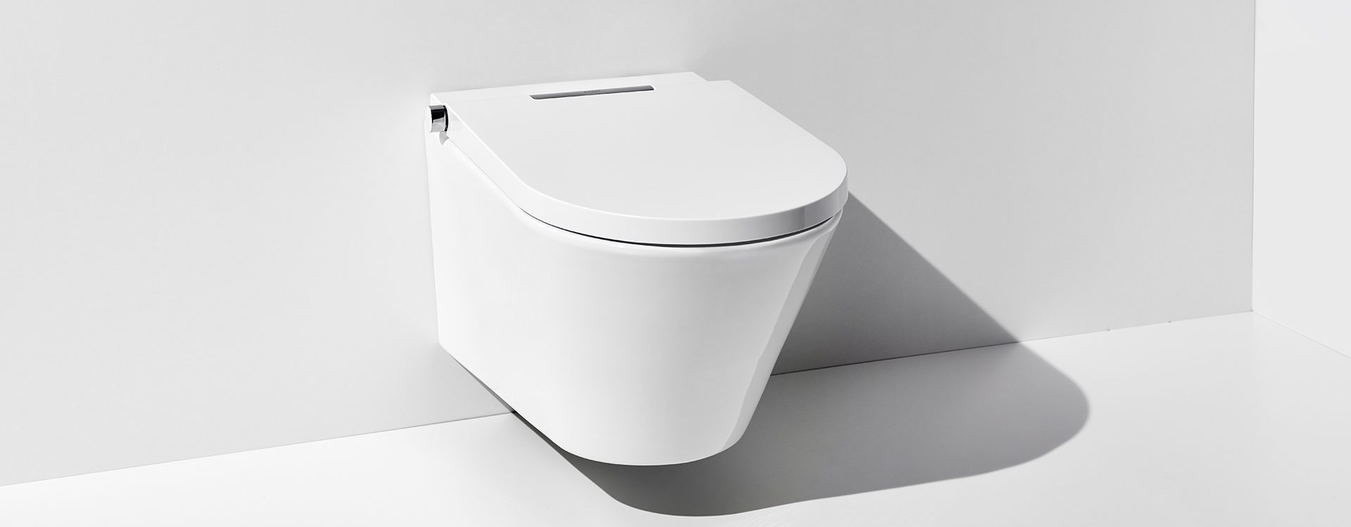 White wall-hung toilet with closed lid and chrome hardware mounted on gray wall.