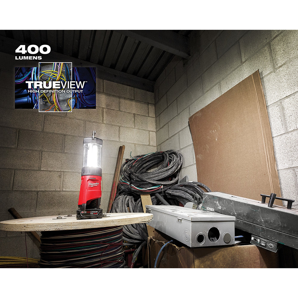 Red and black cordless LED lantern with clear cylindrical top, mounted on battery base, illuminating work area.