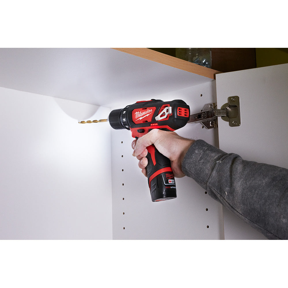 Red and black Milwaukee M12 cordless drill/driver being held while drilling into white cabinet material.