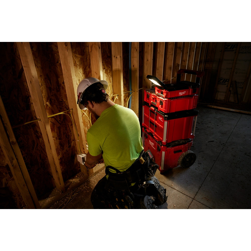 Milwaukee M12 flood light mounted on red PACKOUT toolbox, illuminating work area in indoor construction space.