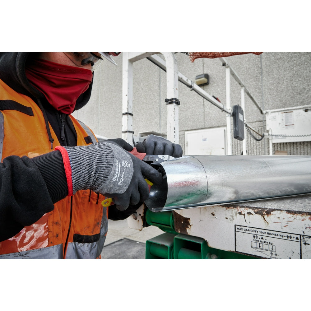 Worker wearing gray and black dipped gloves with red trim handling a metal pipe on a jobsite.