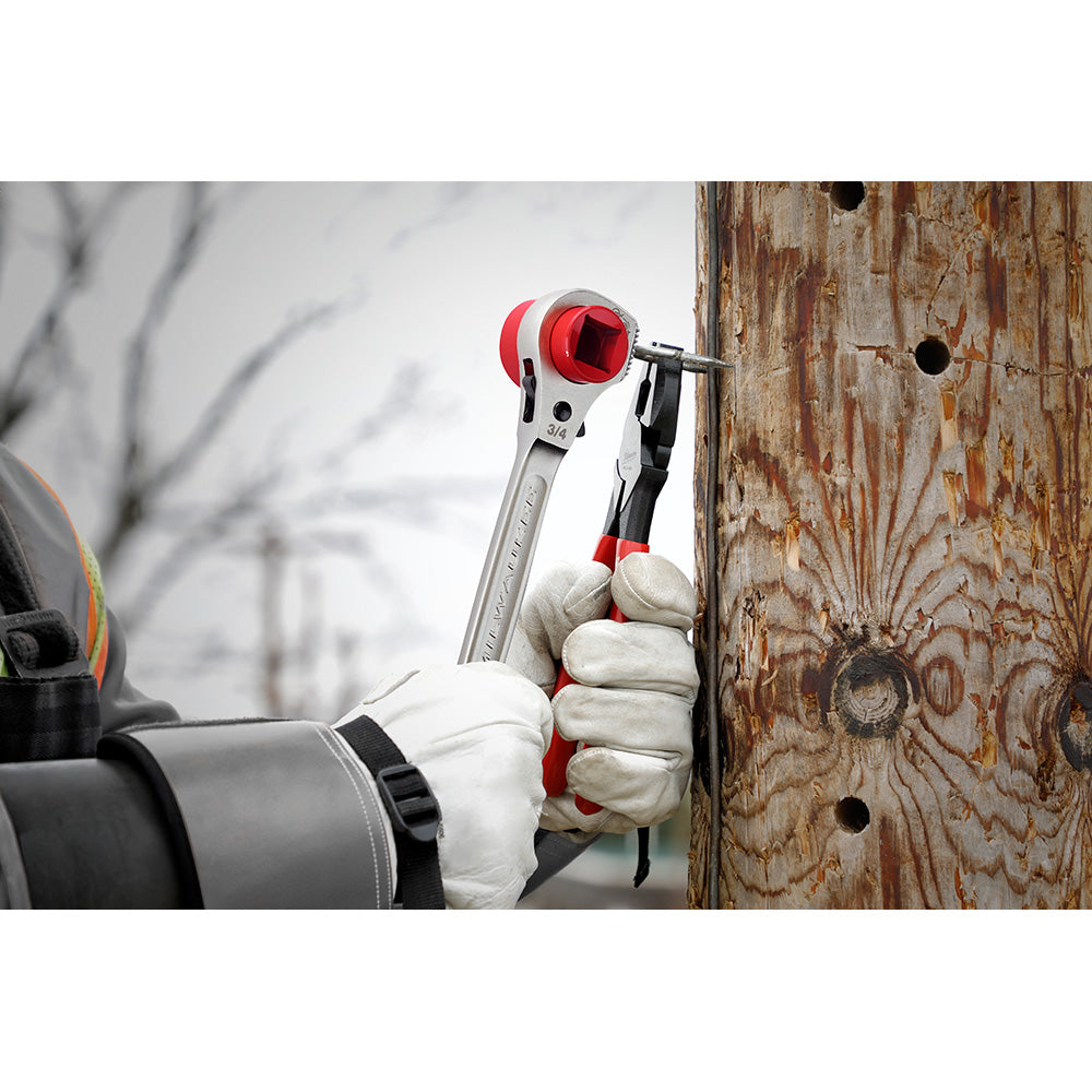 Silver ratcheting wrench with red and black handle held in gloved hand against wooden surface.