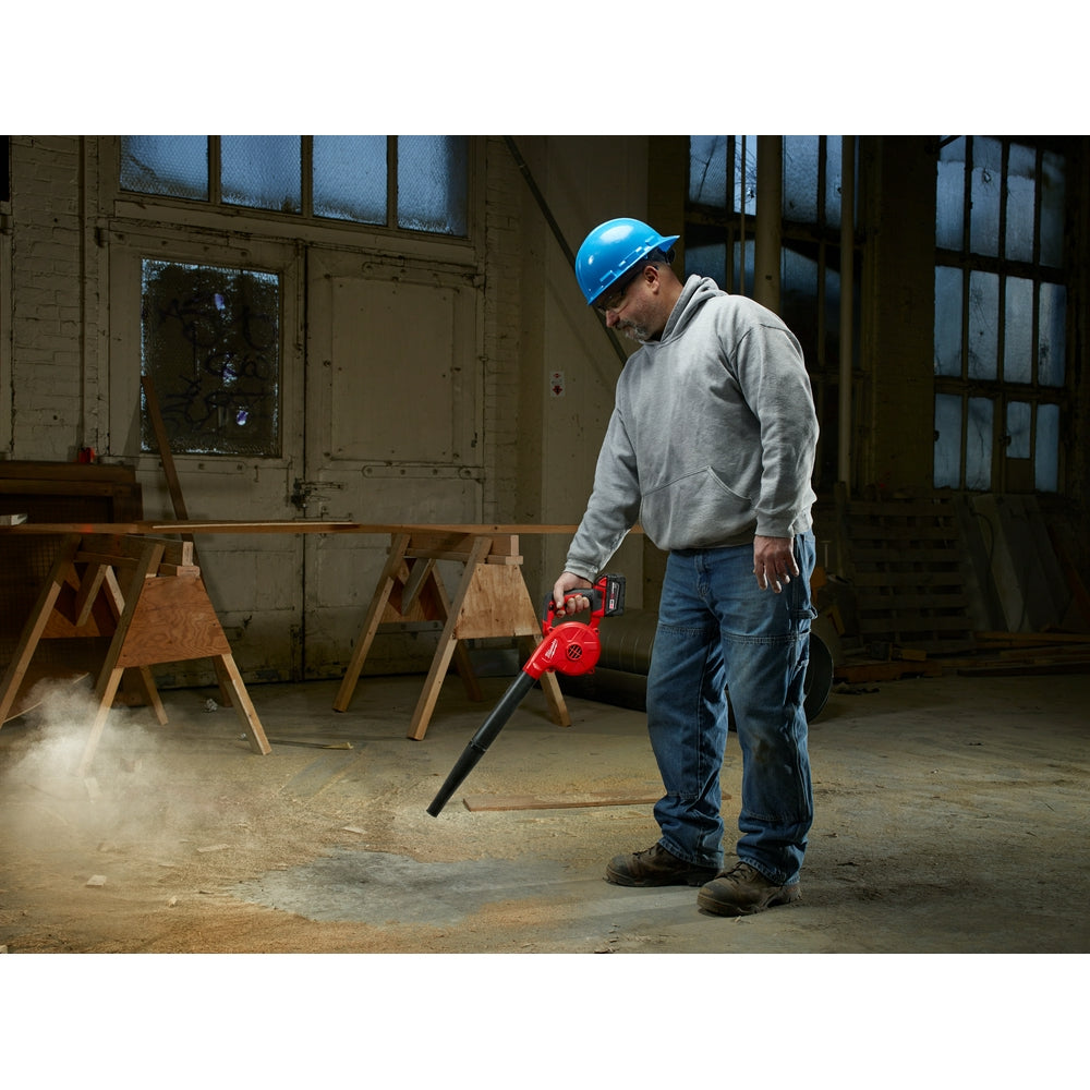 Worker in hard hat operating red and black handheld blower on concrete floor indoors.