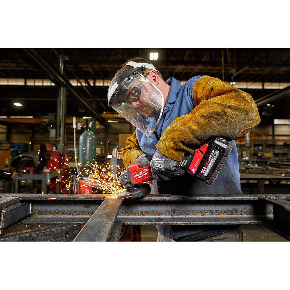 Worker using Milwaukee angle grinder on metal with sparks flying, wearing safety gear and gloves.