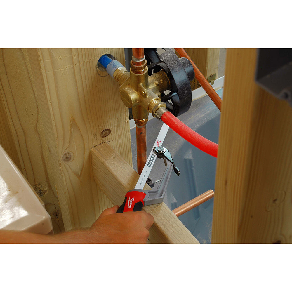 Compact hack saw with red handle and metal frame being held against copper pipe and wooden surface.