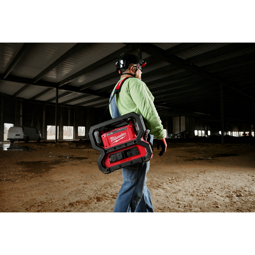 Worker wearing red and black Milwaukee power supply unit on back with shoulder strap across chest.
