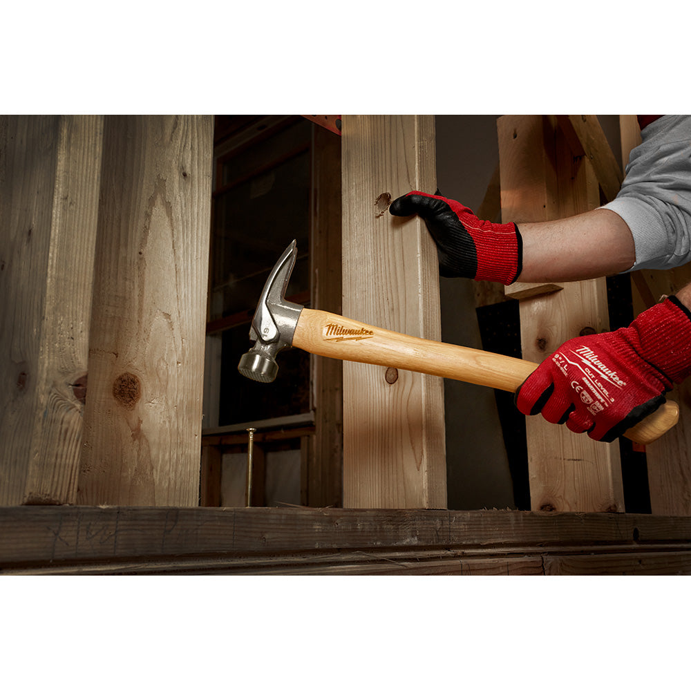 Milwaukee framing hammer with milled face and hickory wood handle being used to drive a nail into wooden framing.
