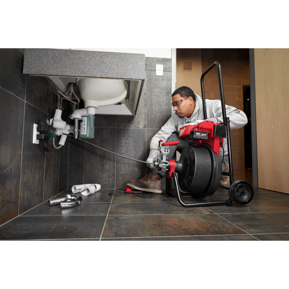 Milwaukee M18 drum machine with cable drive assembly being used to clear a clogged bathroom drain pipe.