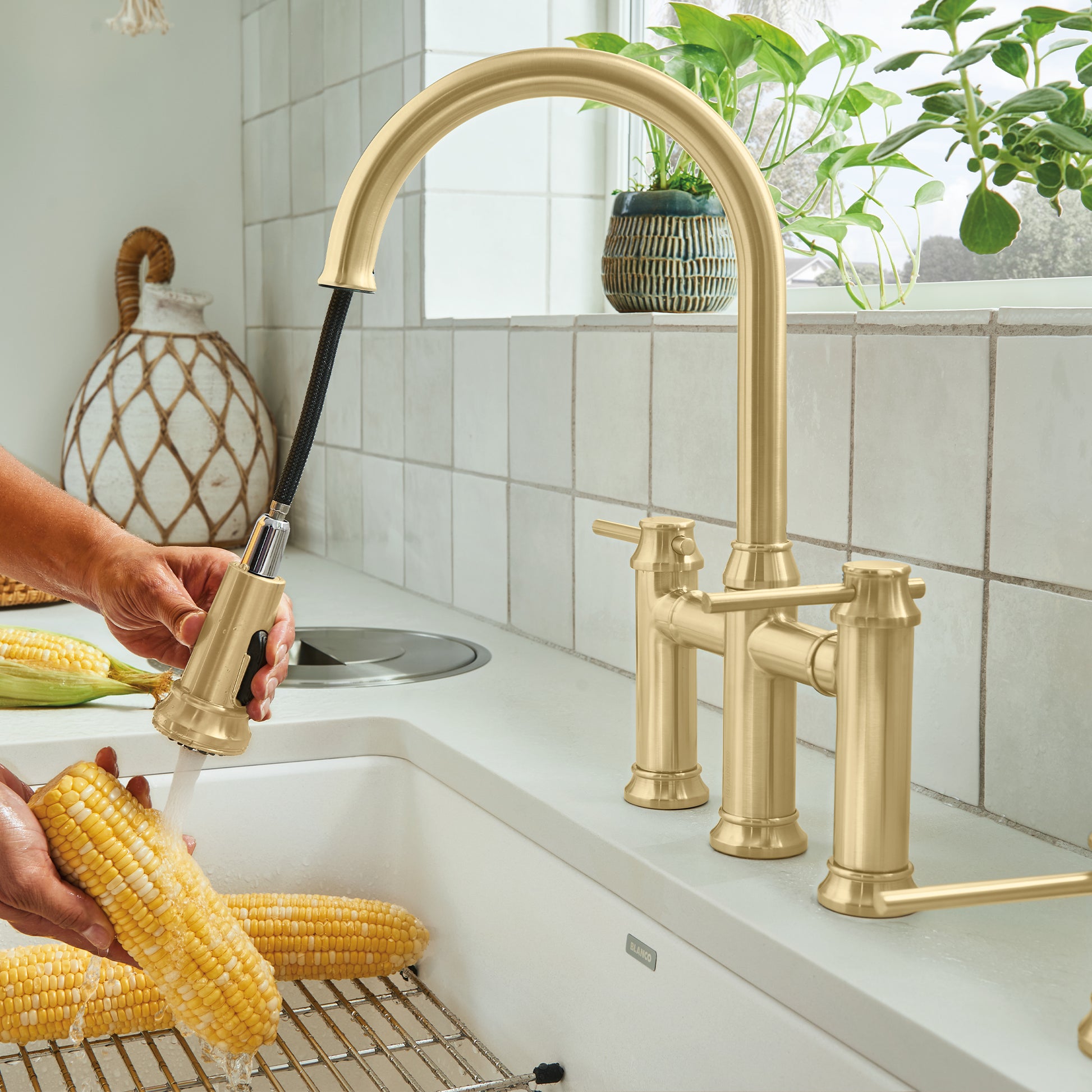 Satin gold bridge faucet with arched pulldown spout, dual handles, and black hose installed on kitchen sink.