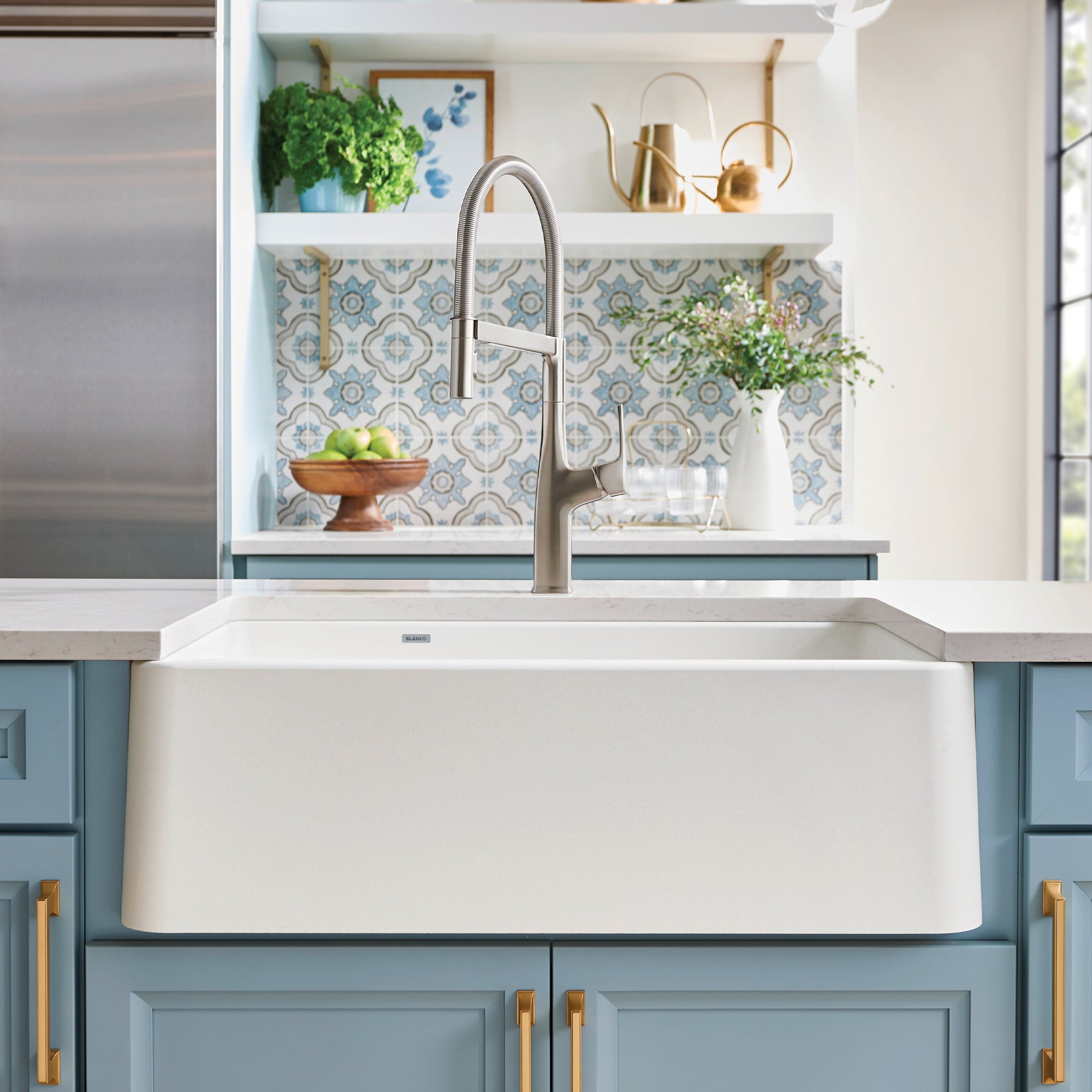 White double-bowl apron farmhouse sink with low divide installed in kitchen cabinetry with stainless steel faucet.