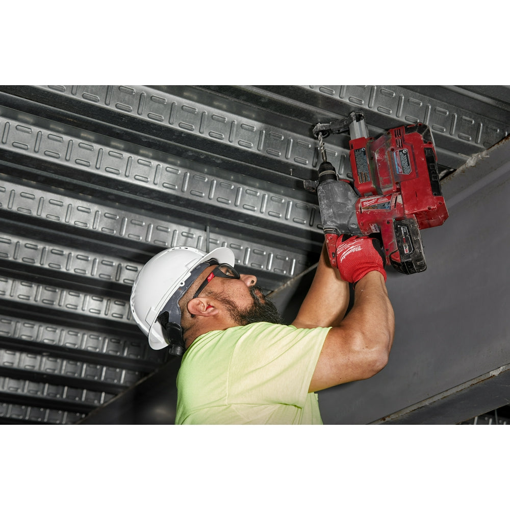 Worker wearing white hard hat and safety glasses installing red Milwaukee power tool on metal ceiling structure.