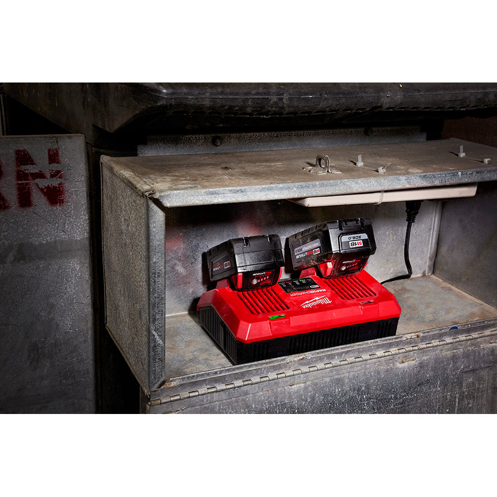 Red and black dual bay charger with two M18 batteries installed on top, positioned in a concrete storage box.