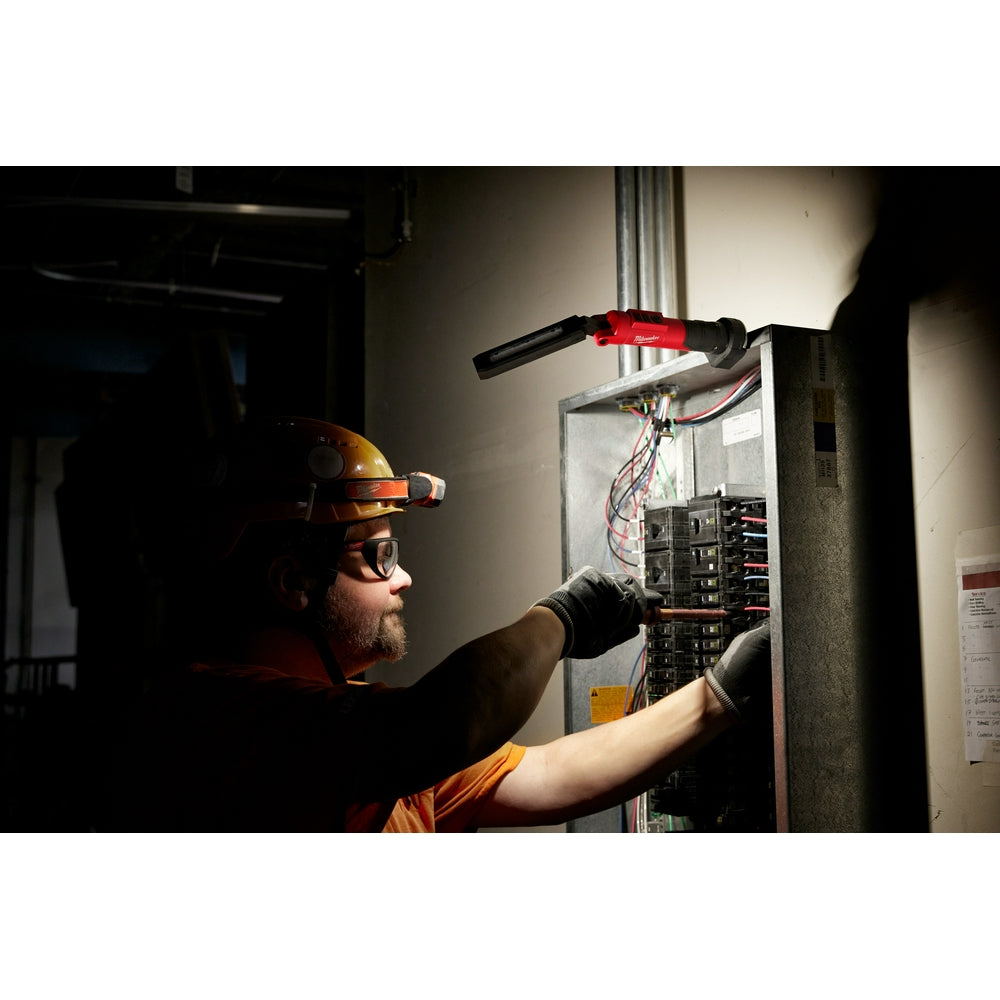 Red and black USB stick light with magnetic base being used by electrician to illuminate electrical panel.
