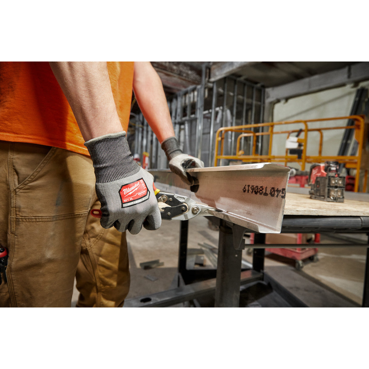 Gray polyurethane-dipped work gloves with Milwaukee branding worn while handling metal sheet in industrial setting.