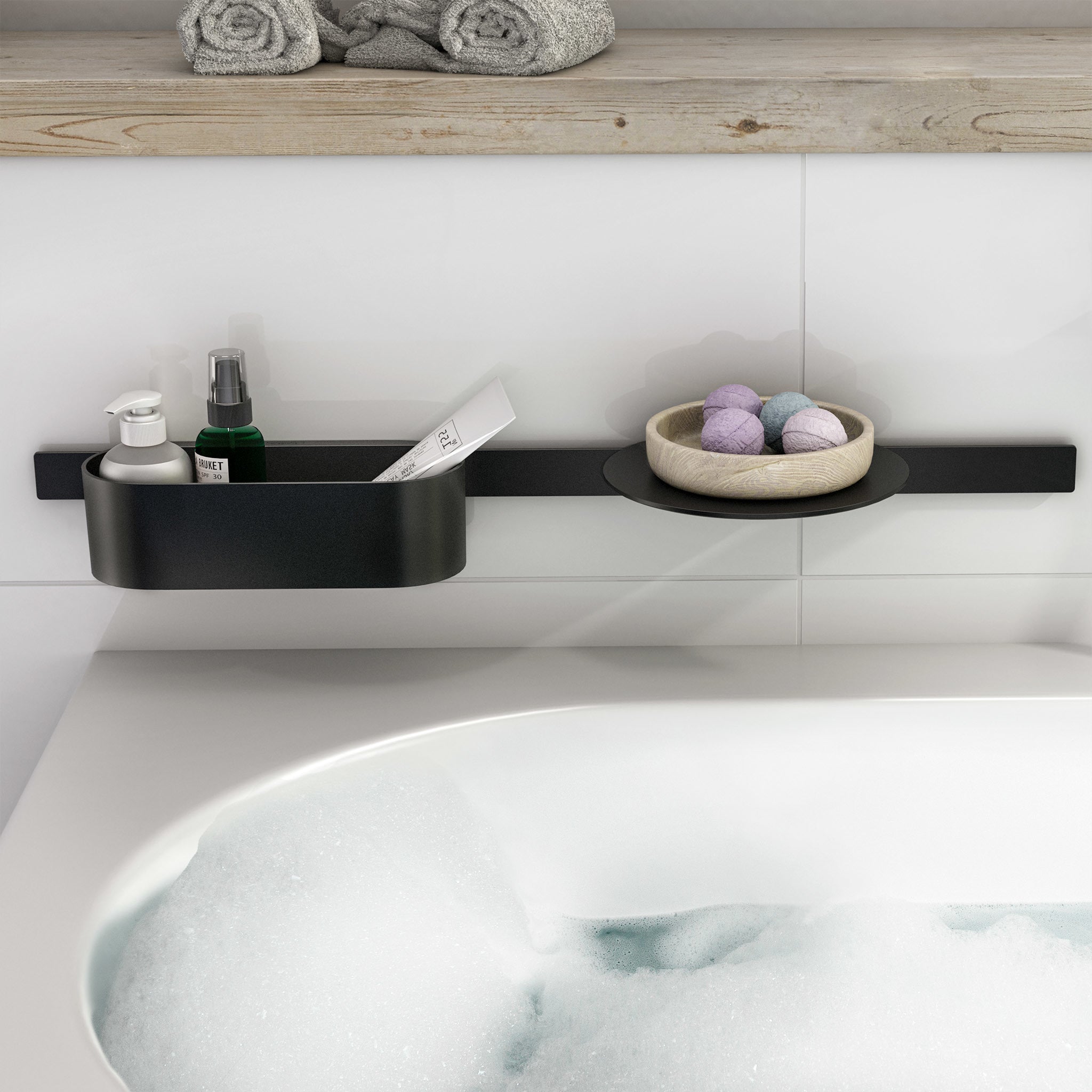 Matte black wall-mounted shelf with integrated storage basin holding bath accessories above a bathtub.